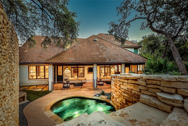 back house at dusk with outdoor lounge area, a patio, and a hot tub