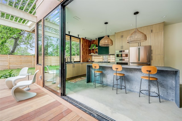 kitchen with appliances with stainless steel finishes, light brown cabinets, pendant lighting, and a healthy amount of sunlight