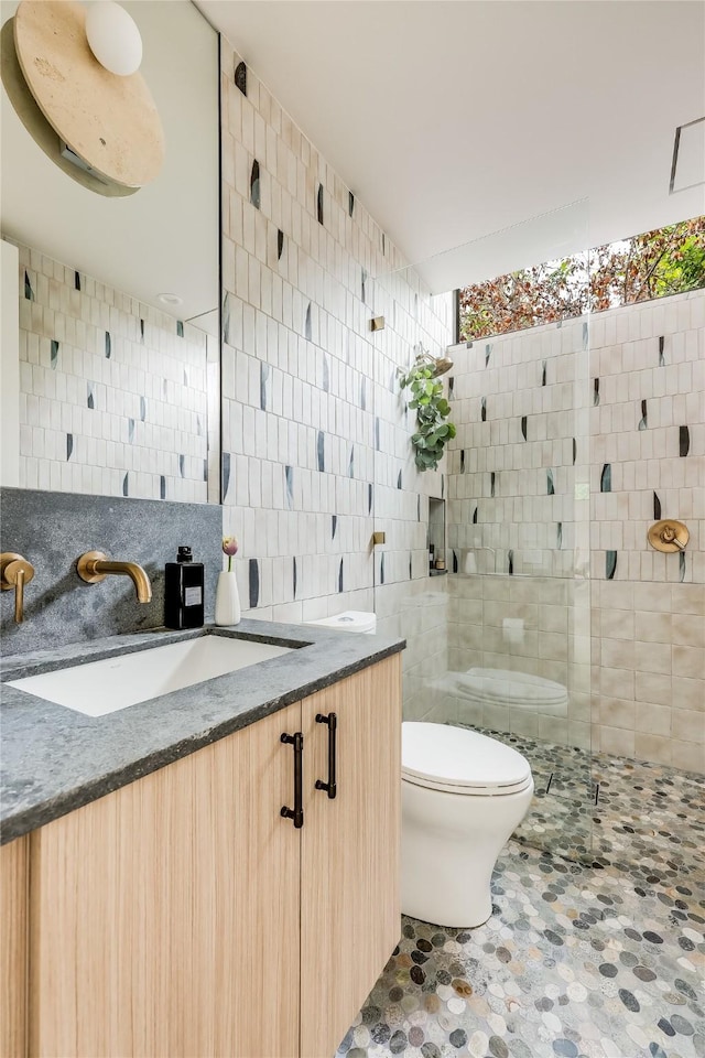 bathroom featuring vanity, backsplash, toilet, tile walls, and a shower with shower door