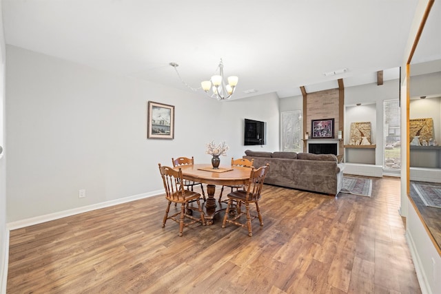 dining space featuring a wealth of natural light, a large fireplace, wood-type flooring, and an inviting chandelier