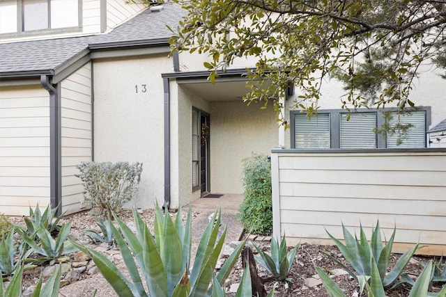 view of exterior entry featuring roof with shingles and stucco siding