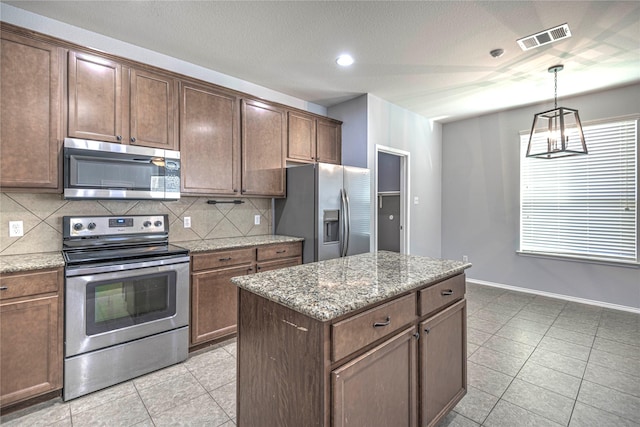 kitchen featuring a kitchen island, decorative light fixtures, backsplash, light stone counters, and stainless steel appliances