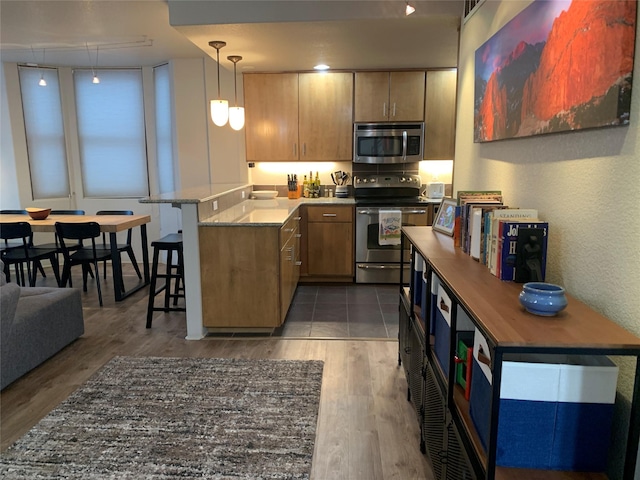 kitchen featuring a kitchen breakfast bar, kitchen peninsula, track lighting, decorative light fixtures, and appliances with stainless steel finishes