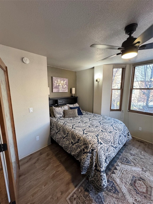 bedroom with ceiling fan, dark hardwood / wood-style floors, and a textured ceiling