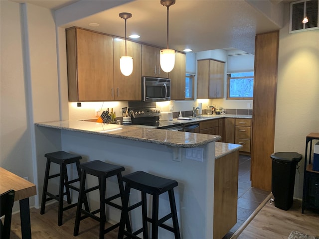 kitchen featuring hanging light fixtures, kitchen peninsula, a breakfast bar area, appliances with stainless steel finishes, and light wood-type flooring