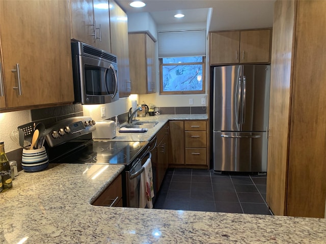 kitchen featuring appliances with stainless steel finishes, light stone counters, dark tile patterned floors, and sink