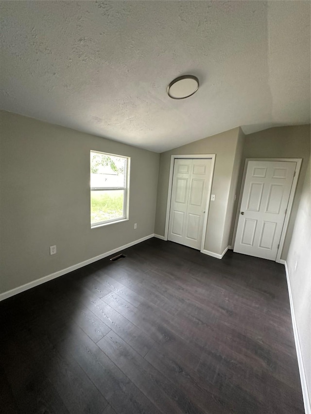 unfurnished bedroom with a textured ceiling, a closet, dark wood-type flooring, and lofted ceiling