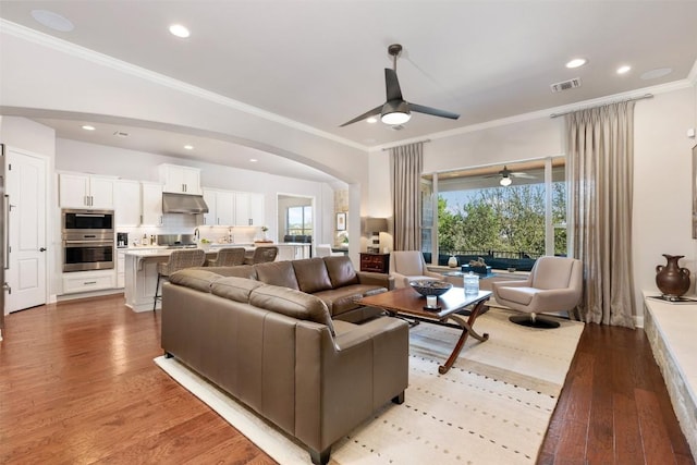 living area featuring visible vents, arched walkways, ornamental molding, light wood-style floors, and recessed lighting