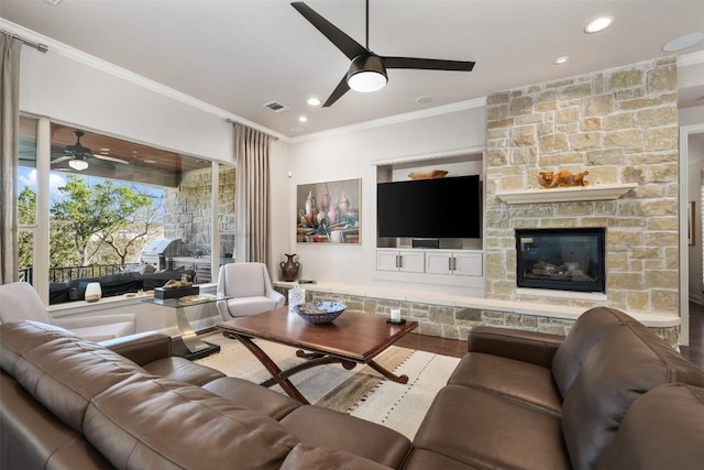 living area featuring a fireplace, visible vents, ornamental molding, a ceiling fan, and wood finished floors