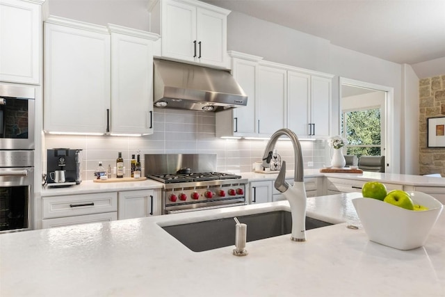 kitchen with white cabinets, under cabinet range hood, tasteful backsplash, and light countertops