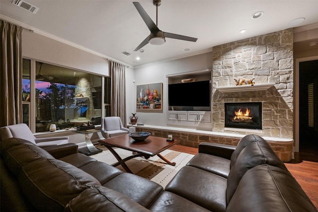 home theater featuring visible vents, ornamental molding, ceiling fan, a stone fireplace, and wood finished floors