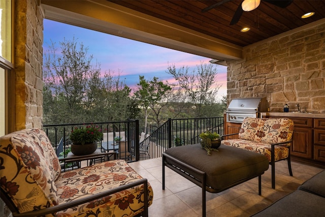 patio terrace at dusk with ceiling fan, exterior kitchen, area for grilling, and a balcony