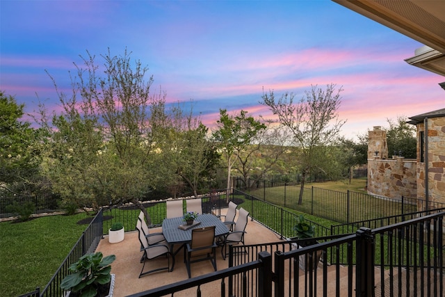 patio terrace at dusk with fence, outdoor dining area, and a lawn