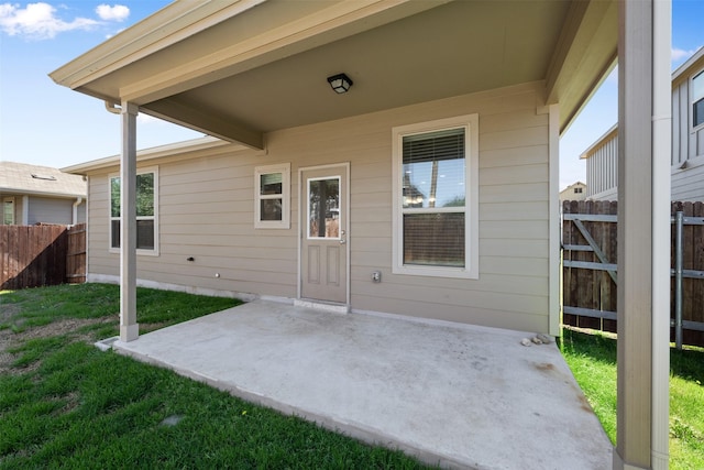 view of exterior entry featuring a patio, a lawn, and fence