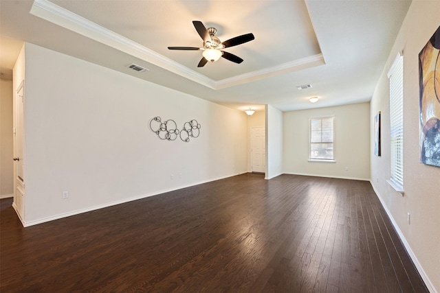 spare room with a tray ceiling, baseboards, visible vents, and dark wood finished floors