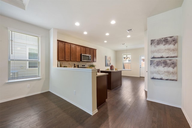 kitchen with a kitchen island, a peninsula, light countertops, dark wood-type flooring, and stainless steel microwave