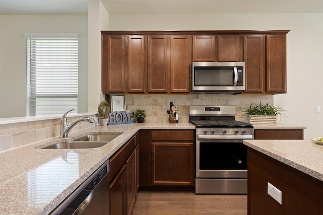 kitchen featuring tasteful backsplash, light stone countertops, stainless steel appliances, and a sink