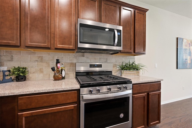 kitchen with backsplash, baseboards, light stone countertops, appliances with stainless steel finishes, and dark wood-style flooring