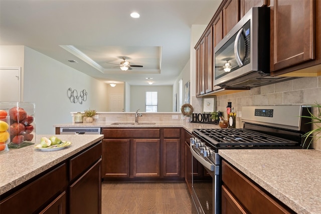 kitchen with light countertops, appliances with stainless steel finishes, wood finished floors, a raised ceiling, and a sink