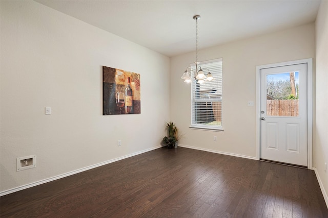 unfurnished dining area featuring a notable chandelier, dark wood-type flooring, and baseboards