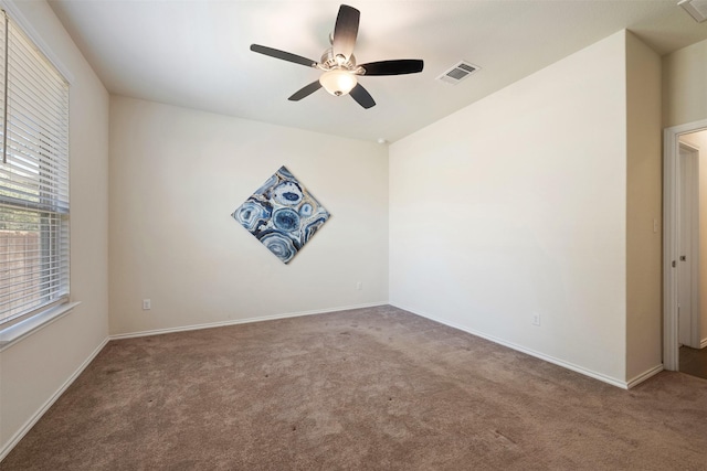 carpeted spare room with visible vents, baseboards, and a ceiling fan