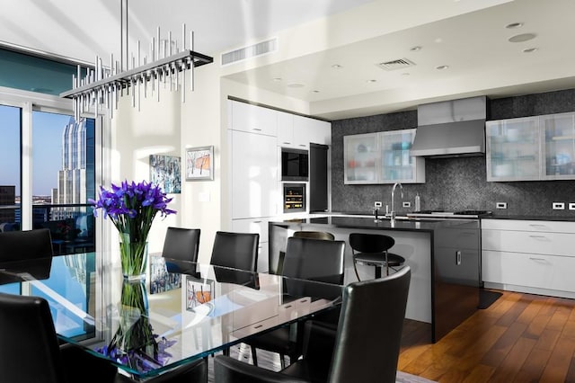 kitchen featuring wall chimney range hood, a kitchen breakfast bar, dark hardwood / wood-style flooring, backsplash, and white cabinets