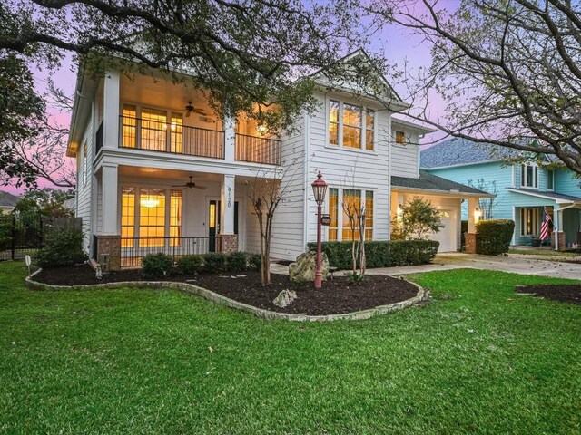 back house at dusk with covered porch, a yard, a balcony, and ceiling fan