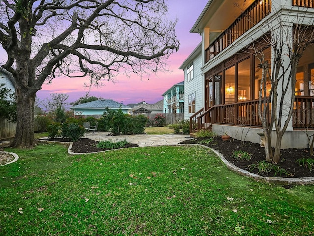 yard at dusk featuring a balcony and a patio