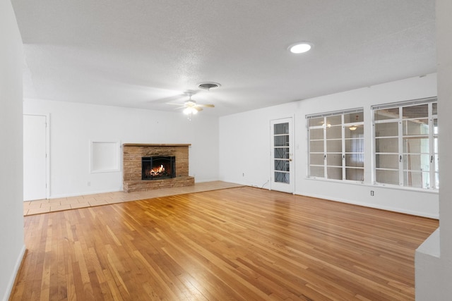 unfurnished living room with hardwood / wood-style floors, a textured ceiling, a stone fireplace, and ceiling fan