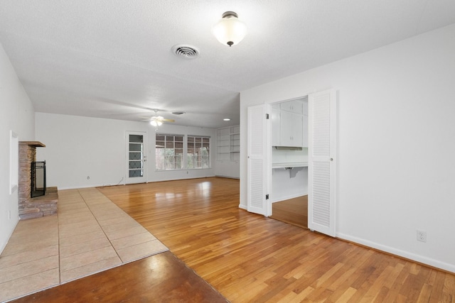 unfurnished living room with ceiling fan, wood-type flooring, a textured ceiling, and a brick fireplace