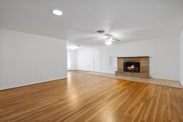 unfurnished living room featuring hardwood / wood-style flooring, ceiling fan, a stone fireplace, and a textured ceiling