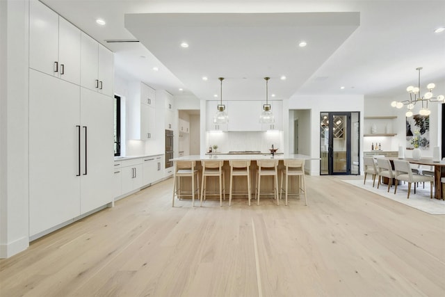 kitchen with a large island with sink, white cabinetry, a breakfast bar, and decorative light fixtures