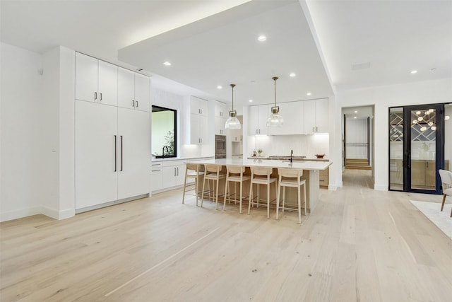 kitchen featuring white cabinetry, light hardwood / wood-style flooring, pendant lighting, a spacious island, and a kitchen bar