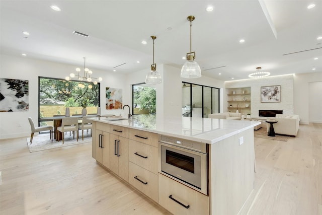 kitchen featuring a large fireplace, a large island, light brown cabinetry, and a chandelier