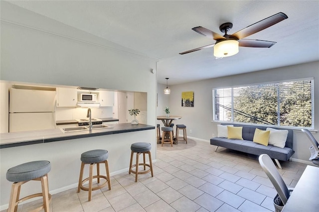 kitchen featuring white appliances, white cabinets, a kitchen breakfast bar, sink, and decorative light fixtures