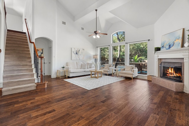 unfurnished living room with dark hardwood / wood-style floors, ceiling fan, a towering ceiling, and a tile fireplace