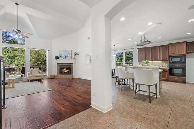 kitchen with black appliances, a kitchen breakfast bar, a center island with sink, ceiling fan, and a wealth of natural light