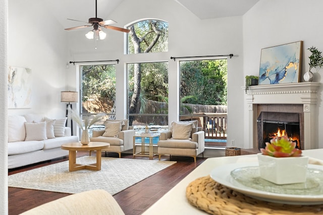 living room featuring dark hardwood / wood-style flooring, high vaulted ceiling, ceiling fan, and a tiled fireplace