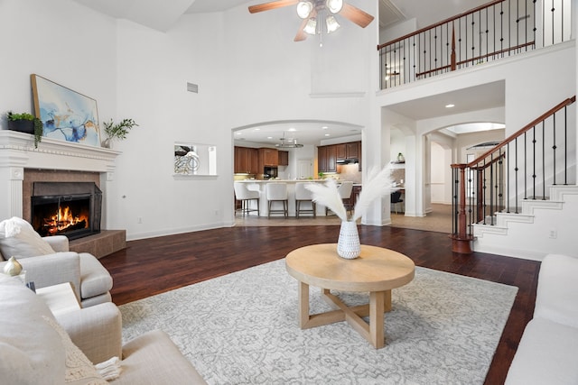 living room featuring a tiled fireplace, ceiling fan, a towering ceiling, and dark hardwood / wood-style floors