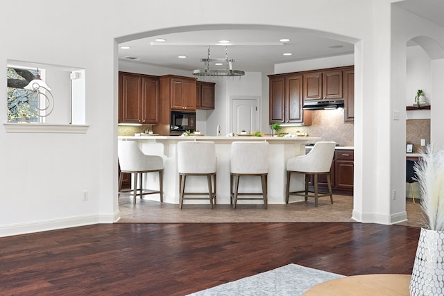 kitchen with a kitchen bar, backsplash, black microwave, and dark hardwood / wood-style flooring