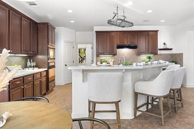 kitchen with black oven, light tile patterned floors, a kitchen island with sink, and a breakfast bar