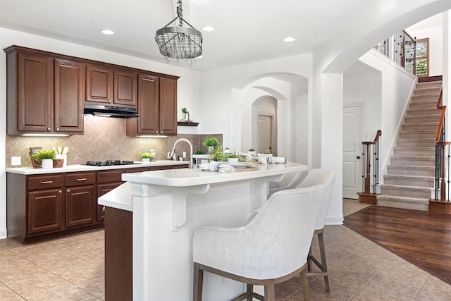 kitchen with hanging light fixtures, a kitchen breakfast bar, black gas cooktop, a center island with sink, and light tile patterned flooring