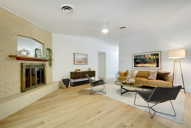 living room with ceiling fan, light hardwood / wood-style floors, vaulted ceiling, and a brick fireplace