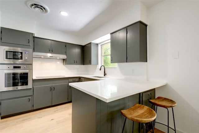 kitchen featuring kitchen peninsula, appliances with stainless steel finishes, a breakfast bar, sink, and gray cabinets