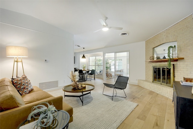 living room featuring ceiling fan, light wood-type flooring, lofted ceiling, and a brick fireplace