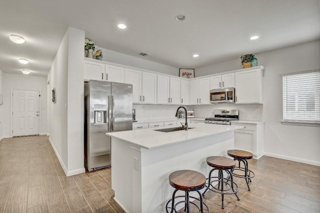 kitchen featuring sink, appliances with stainless steel finishes, white cabinetry, a kitchen island with sink, and tasteful backsplash