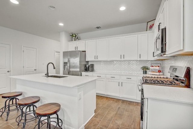 kitchen with sink, tasteful backsplash, a center island with sink, appliances with stainless steel finishes, and white cabinets