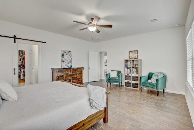 bedroom featuring ceiling fan, a barn door, and light wood-type flooring