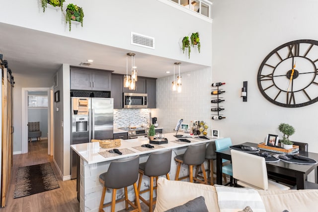 kitchen featuring kitchen peninsula, appliances with stainless steel finishes, a kitchen bar, decorative light fixtures, and light hardwood / wood-style floors