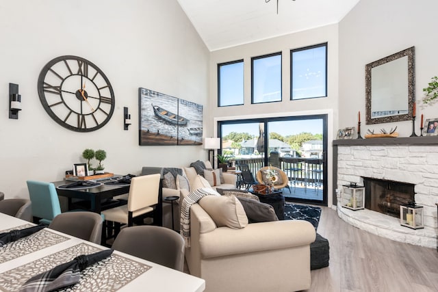 living room featuring high vaulted ceiling, light hardwood / wood-style flooring, and a stone fireplace